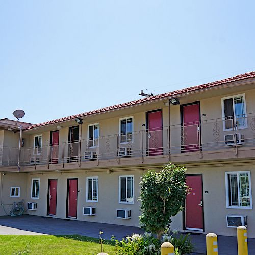 The image shows a two-story motel with red doors, beige walls, and air conditioners in some windows. There is a vending machine on the left.