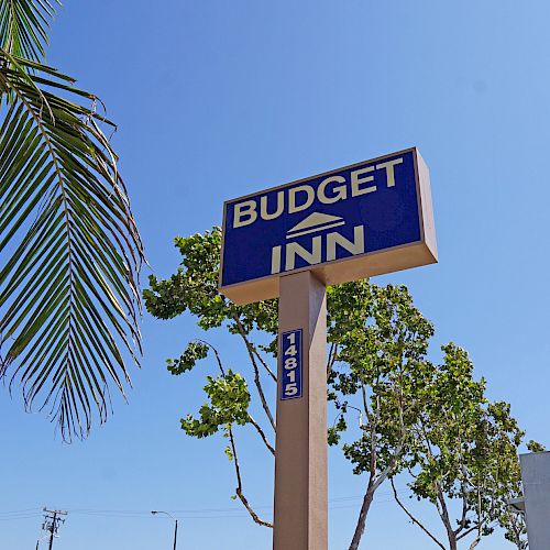 This image shows a "Budget Inn" sign against a clear blue sky, with trees and part of a building in the background.