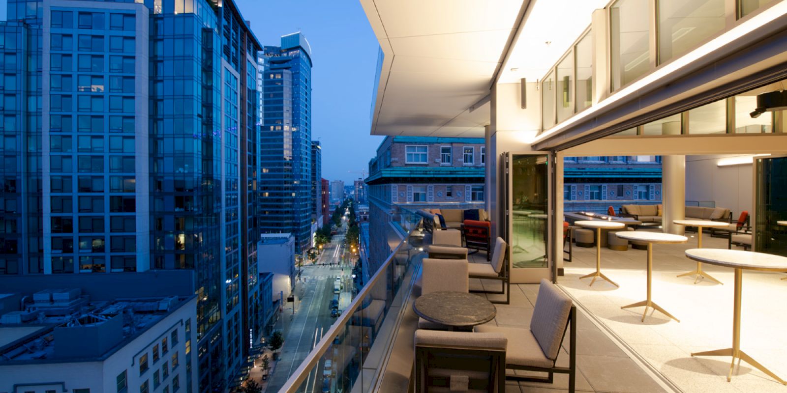 The image shows a modern cityscape at dusk with tall buildings. It also features an outdoor patio area with seating and tables.