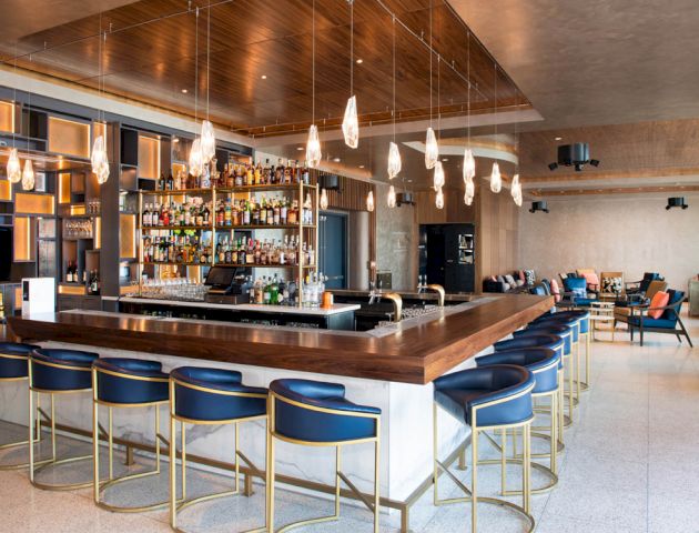 A modern bar with a variety of bottles on shelves behind it, stylish stools at the counter, and comfortable seating areas in the background.