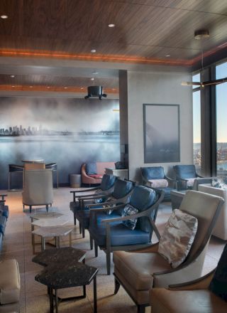 A modern lounge with comfortable seating, large windows offering a scenic view, and a wall mural of a city skyline.
