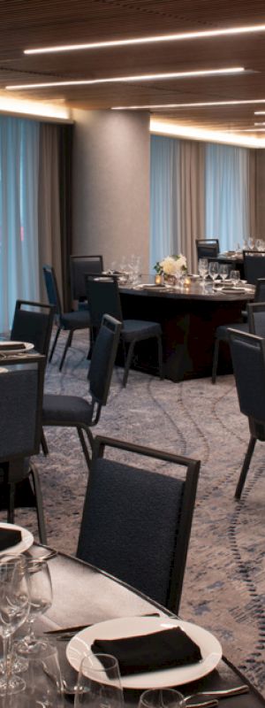 The image shows an elegantly arranged banquet hall with round tables set for a formal event, adorned with black napkins and floral centerpieces.