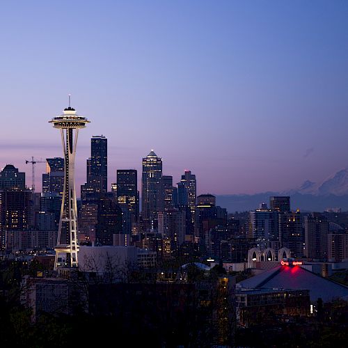 The image shows the Seattle skyline at dusk, with the Space Needle prominently lit and Mount Rainier in the background.
